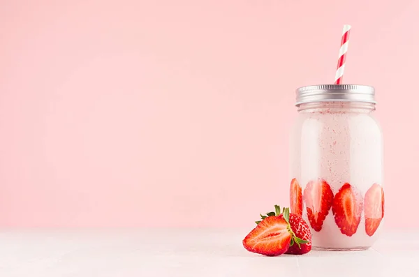 粉红草莓冰沙与片多汁的水果在复古罐子与红色条纹秸秆在轻软柔和的粉红色墙壁和白色木桌 复制空间 — 图库照片