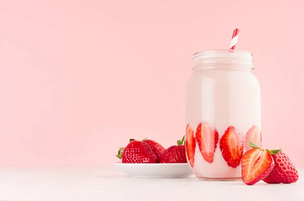 新鲜草莓牛奶甜点早餐在罐子与成熟的浆果在茶托 秸秆在柔和的粉红色墙壁和白色木桌 特写镜头 — 图库照片