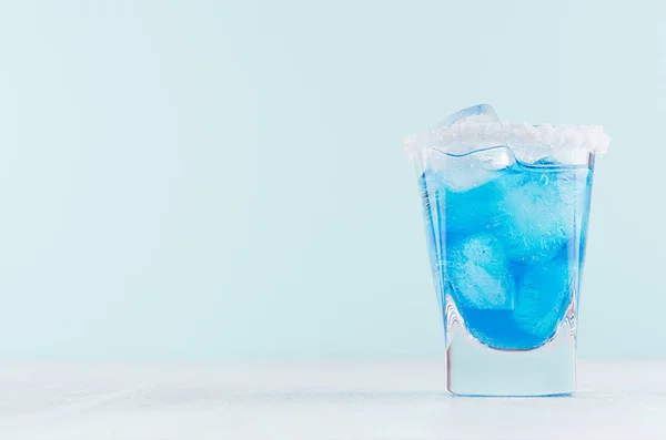 热带新鲜酒精鸡尾酒与蓝色 Curacao 利口酒 盐边缘在冻结的射击玻璃在柔和的轻白色 柔和的绿色背景 — 图库照片