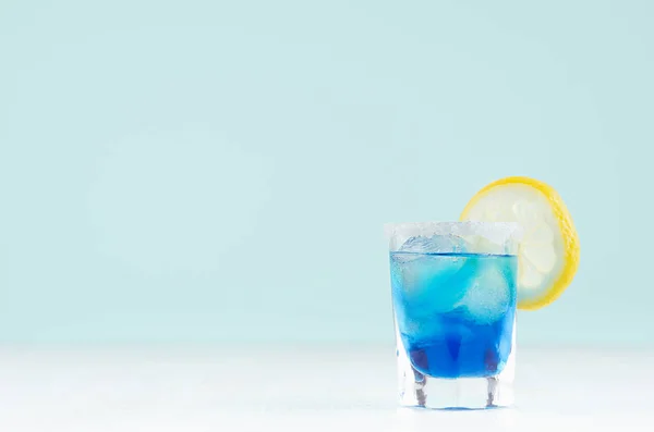 热带新鲜酒精鸡尾酒与蓝色库拉索利口酒 糖边缘 柠檬在雾化射玻璃杯软淡白色 柔和的绿色背景 — 图库照片