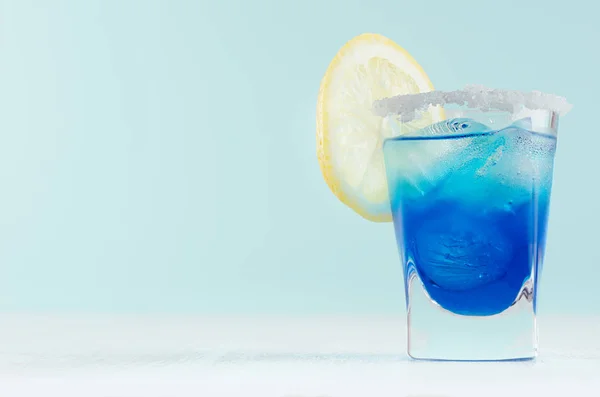 蓝色库拉索鸡尾酒与柠檬片 糖边缘在优雅的白色木板和柔和的薄荷彩墙拍摄玻璃 — 图库照片