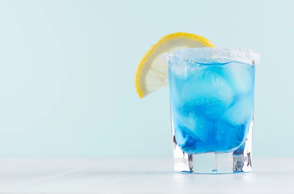 异国情调的冷射玻璃鸡尾酒 蓝色库拉索 柠檬片在柔和的薄荷颜色背景和白色木板 — 图库照片