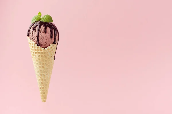 チョコレートソースとワッフルコーンのブラウンクリーミーなアイスクリームスクープ ピンクの背景に緑のミントの葉 — ストック写真