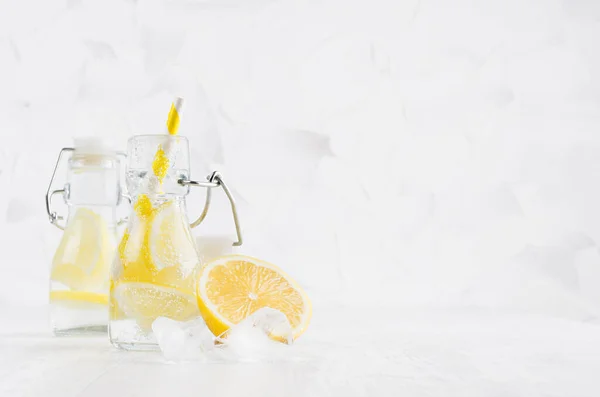 Fresh summer cocktails with sour lemon, soda, ice cubes, straw in yoke bottles on elegant soft light white wooden board and plaster wall.