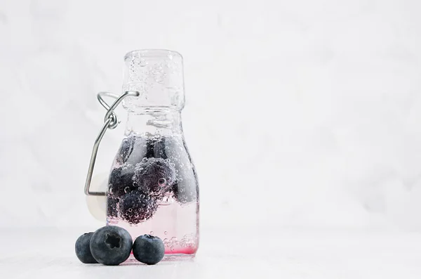Summer homemade pink drink - infused blueberry water with berry, soda in yoke bottle in soft light white interior, copy space.