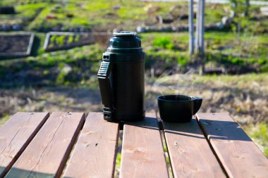 Termos ve bir kupa, çardağın ahşap masasında sıcak çay. Yaz pikniği, açık hava aktiviteleri..