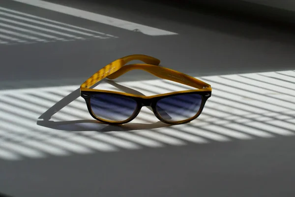 Κοντινό πλάνο κίτρινο με μαύρα γυαλιά ηλίου. μια σκιά από τις περσίδες πέφτει στα γυαλιά — Φωτογραφία Αρχείου