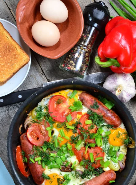 Huevos revueltos con salchichas fritas, cebollas, pimientos rojos dulces, todo en una sartén. —  Fotos de Stock