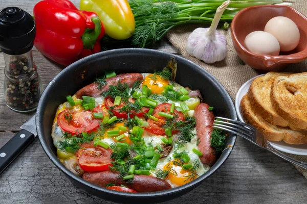 Huevos revueltos con salchichas fritas, cebollas, pimientos rojos dulces, todo en una sartén. —  Fotos de Stock