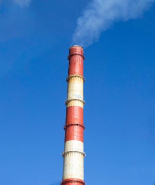 Mavi gökyüzüne karşı fabrikanın paslı duman piposu endüstriyel pipo bacasından beyaz duman çıkıyor. Fabrikanın etrafındaki temiz hava. Üretim fabrikasında çevre yönetimi.