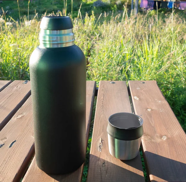 Черный термос и кружка с горячим чаем на деревянном столе во время загородного отдыха. концепция отдыха на свежем воздухе, — стоковое фото