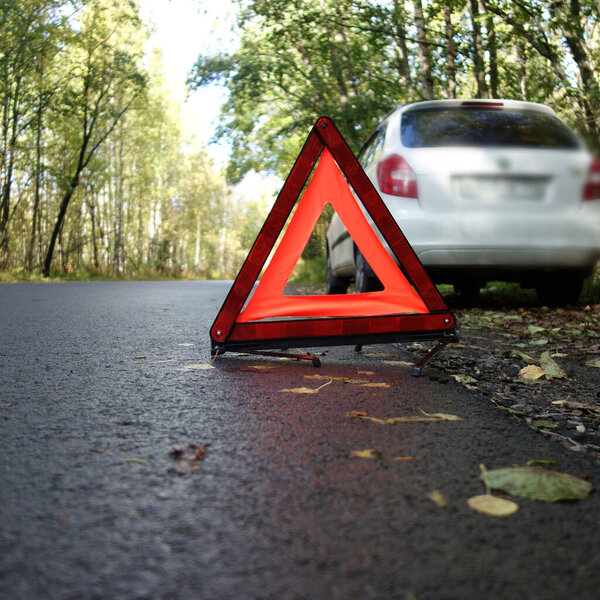 set emergency stop sign on the road in autumn forest, background white car. concept of roadside and travel assistance. close-up