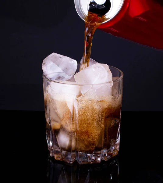 man pours soda from an aluminum red can into a glass with ice, against a dark background. The drink is produced and manufactured by famouse copmpany. copy space.