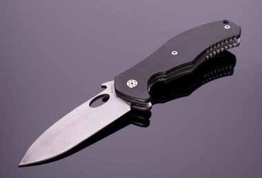 Koyu arka planda izole edilmiş, parlak yüzeyde yansıması olan çelik saplı, desenli siyah plastik kaplama plakalı, katlanmış bir cep çakısı. Cep çakısı yakın çekim görüntüsü