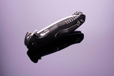 Kapalı katlanmış çakı, desenli siyah plastik kaplama plakalar, koyu arka planda izole edilmiş, parlak yüzeyde yansıması var. Cep çakısı yakın çekim görüntüsü