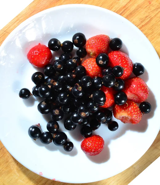 Φράουλες Και Μαύρα Φραγκοστάφυλα Λευκό Πιάτο Και Ξύλινο Τραπέζι Συγκομιδή — Φωτογραφία Αρχείου