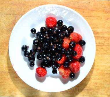 Beyaz tabakta çilek ve siyah frenk üzümü ve ahşap masa, taze ve vitamin zengini yiyecekler. düz yat