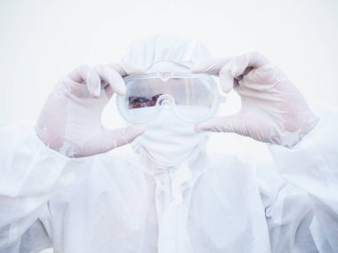 Asya 'lı genç doktor ya da PPE süit üniformalı bilim adamı iki eliyle gözlük tutarken geleceğe bakıyor. Coronavirus veya COVID-19 kavramı izole edilmiş beyaz arkaplan