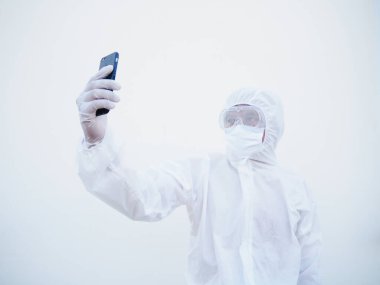 PPE süit üniformalı genç bir doktor ya da bilim adamı telefonunu selfie çekmek ve aile veya Freind ile görüntülü sohbetler yapmak için kullanıyordu. Coronavirus veya COVID-19 kavramı izole edilmiş beyaz arkaplan