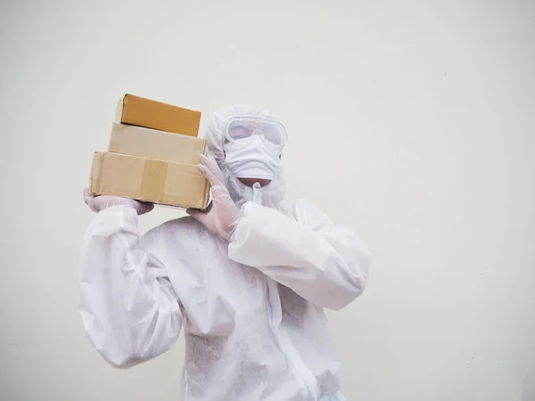 Young man in PPE suite uniform while holding cardboard boxes in medical rubber gloves and mask. coronavirus or COVID-19 concept isolated white background