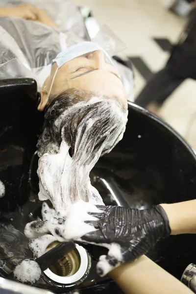 Hairdressing services during the coronavirus. Hands of hairdresser washing head of woman in mask. Hairdresser washing head of woman