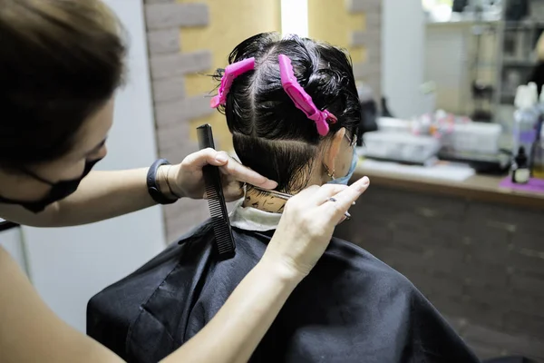 Hairdressing services during coronavirus. Hairdresser in face mask cuts hair of woman in face mask. Hairdressers cutting hair during COVID-19