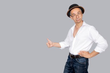 Şapkalı, gözlüklü ve beyaz gömlekli çekici bir adam portresi. Adam tamam işareti gösteriyor. Erkek, parmaklarıyla iyi jest yapıyor. İzole edilmiş gri arka plan. Vücut dili kavramı. Boşluğu kopyala