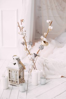 Beyaz ahşap zemin penceresi olan büyük, temiz, parlak bir oda, lale perdeleriyle süslenmiş bir yatak, pamuk dallarla süslenmiş vazolar.