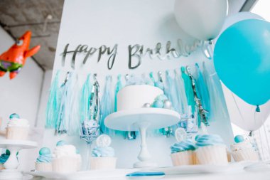 Bir yaşındaki erkek bebeğin onuruna şenlikli bir dekor. Kürsüde beyaz pasta, kekler, mavi toplar ve süslemeler. 