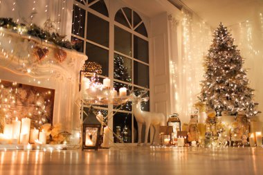 Noel iç tasarımında sıcak ve sıcak bir akşam, ışıklarla süslenmiş Xmas ağacı hediyeler, oyuncaklar, geyikler, mumlar, fenerler, kapalı alanda yanan çelenkler.
