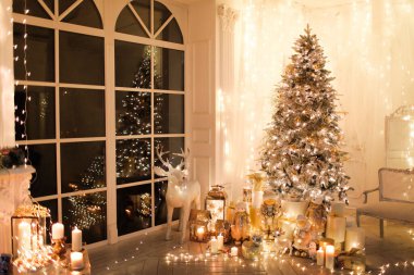 Noel iç tasarımında sıcak ve sıcak bir akşam, ışıklarla süslenmiş Xmas ağacı hediyeler, oyuncaklar, geyikler, mumlar, fenerler, kapalı alanda yanan şömine. tatil salonu sihirli yeni yıl