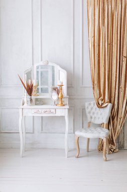Güzel, beyaz bir iç mekan. Ahşap zemin aydınlatma duvarlı klasik oda pervazlı sandalye aynalı tuvalet masası, altın elementlerle süslenmiş.