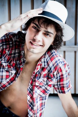 Gömleği, kotu ve şapkası olan çıplak vücutlu, neşeli, esmer bir genç.