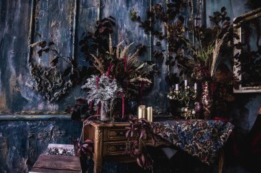 Kurumuş çiçekler, vazolar, avizeler, altın çerçeveli kumaşlar, lüks kraliyet tarzı ahşap bir masa, eski fenerlerle yanan mumlar.