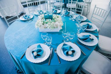 Düğünde mavi ve beyaz renklerde güzel dekore edilmiş restoranlar masa örtüleriyle servis edilen masa örtüleri, tekstil peçeteleri vazolarda mavi suyla servis edilen çiçekler.