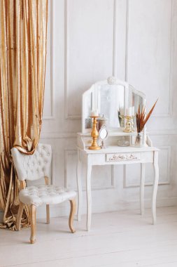 Güzel, beyaz bir iç mekan. Ahşap zemin aydınlatma duvarlı klasik oda pervazlı sandalye aynalı tuvalet masası, altın elementlerle süslenmiş.