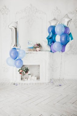 Çocuğun ilk doğum gününü kutlamak için şömineli ve mavi balonlu beyaz bir oda.
