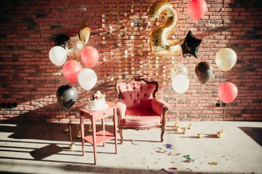 Çocuk doğum günü şerefine 2 yıl, stüdyo dairede, güneş ışığıyla dolu. Klasik turuncu sandalye, pasta masası, kırmızı, siyah, altın balonlar tuğla duvar zemininde