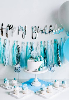 Bir yaşındaki erkek bebeğin onuruna şenlikli bir dekor. Kürsüde beyaz pasta, kekler, mavi toplar ve süslemeler. 