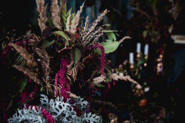 Kurumuş çiçekler, vazolar, avizeler, altın çerçeveli kumaşlar, lüks kraliyet tarzı ahşap bir masa, eski fenerlerle yanan mumlar.