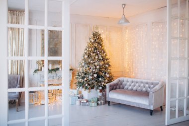 Noel ağacı ve dekoratif şömineyle süslenmiş, zarif, aydınlık renkte bir oda tasarımı.