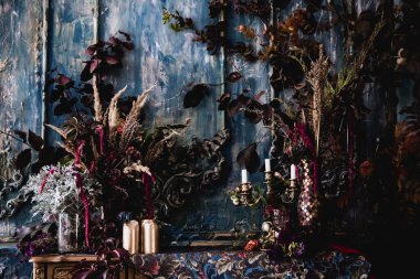 Kurumuş çiçekler, vazolar, avizeler, altın çerçeveli kumaşlar, lüks kraliyet tarzı ahşap bir masa, eski fenerlerle yanan mumlar.