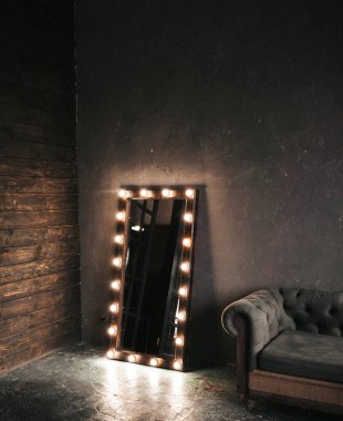 Köşe odasında ahşap ve gri beton bir duvar, yaşlanmış bir zemin, siyah cam kapılar ve ampullü elektrikli makyaj aynası ve tavan arası tarzı Oxford kanepesi.