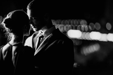 Şık giyinmiş zarif bir çift akşam vakti dışarıda sarılıyor.