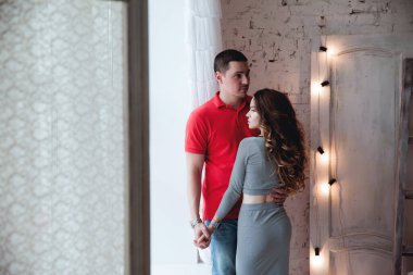 Evde pencerenin yanında genç bir çift sarılıyor.