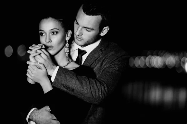 Şık giyinmiş zarif bir çift akşam vakti dışarıda sarılıyor.