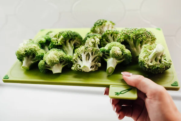 Kadın eli kesme tahtasıyla yeşil brokoli tutuyor.