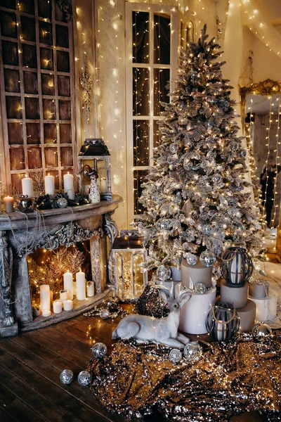 warm and cozy evening in Christmas interior design,Xmas tree decorated by lights presents gifts,toys, deer,candles, lanterns, garland lighting indoors fireplace.holiday living room.magic New year