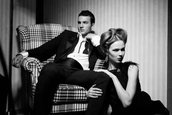 在房间的阴影中 穿着经典衣服的年轻貌美的情侣们 坐在椅子上的女人 在她脚边的男人 — 图库照片