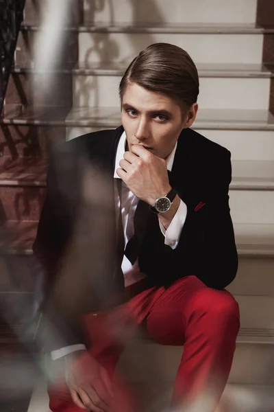 赤いズボンを着たハンサムな男と階段に座っている黒いジャケット — ストック写真